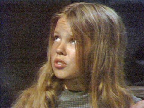 Head and shoulders shot of Kylie Minogue at age 8 in an episode of The Sullivans. She is looking upwards, away from the camera and her hair is partly covering her face.