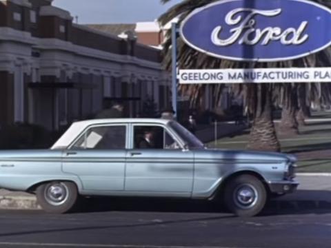 A blue car, in front of a sign reading 'Ford Geelong Manufacturing Plant'