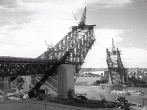 Sydney Harbour Bridge under construction with cranes on top. The two arches of the bridge are coming together but there's still quite a way to go until they meet.