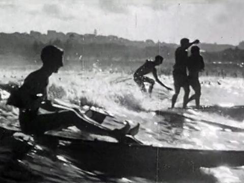 Silhouette of surfers and kayakers riding waves at Bondi Beach in 1929.