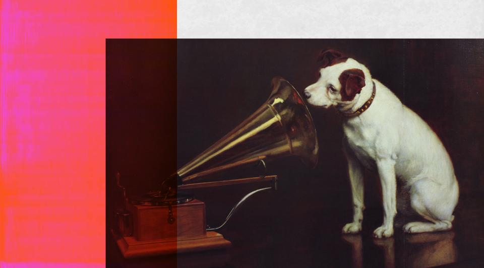 A terrier dog sitting next to a gramophone and putting his nose into the horn. 