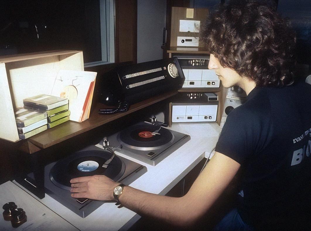 Radio and TV personality Lee Simon sitting in a radio studio in front of some turntables. He is turned slightly away from the camera.