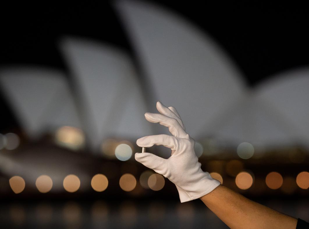 Hand holding a small metal capsule of DNA with the Sydney Opera House in the background