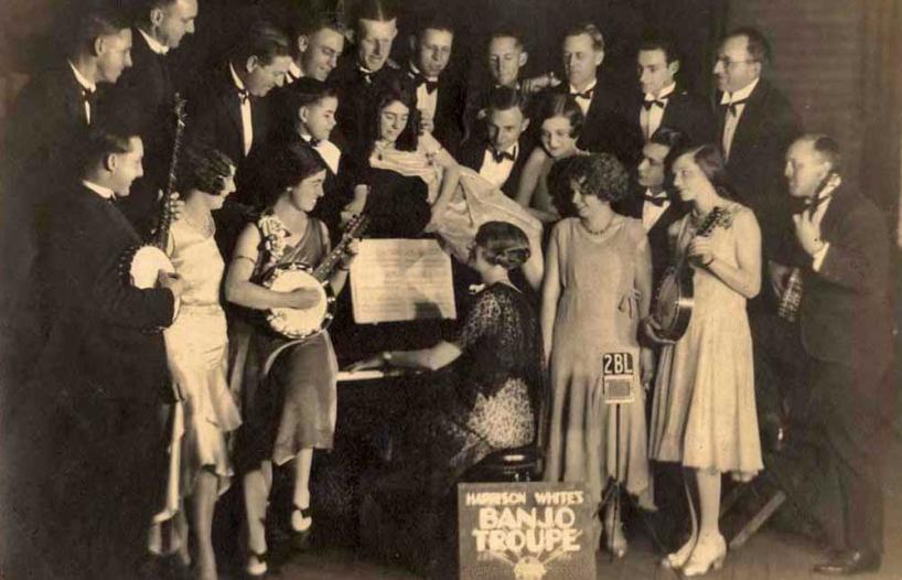 A group of people holding banjos and standing around a piano.