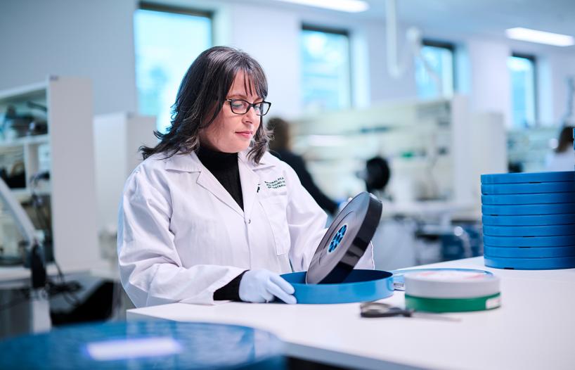 Woman in a lab coat removing a film reel from its container