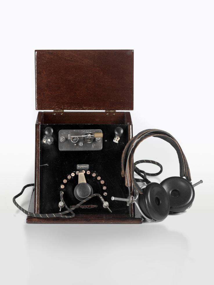 A radio receiver from the 1920s, housed in a wooden box with a set of headphones attached to it.