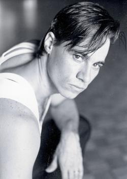 Paul Mercurio in a Strictly Ballroom publicity shot, crouching down on the floor with one elbow resting on his knee and looking sideways towards the camera.