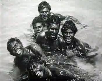 A group of Aboriginal men swimming and laughing as they look at the camera.