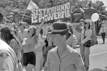 A women's liberation march on the streets of Sydney. Hundreds of women on the street. Some are holding a large sign that says 'Sisterhood is powerful'.