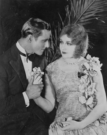 A dashing young man proposes to a young woman in a sequinned dress