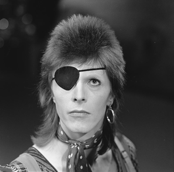 David Bowie wears an eye patch on one eye. He is looking up.