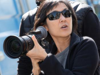 A woman pictured from the chest up holding a camera with a long lens and wearing sunglasses.