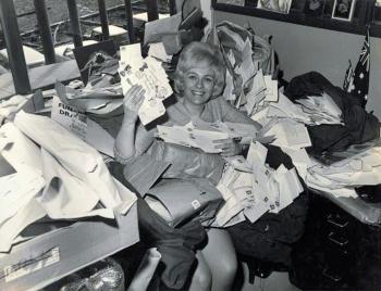 A woman sitting in an office surrounded by letters. She is smiling at the camera and holding some of the letters up.