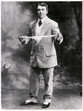 Portrait of Billy Williams as a young man wearing a light coloured suit and twirling a hankerchief bewteen both hands.