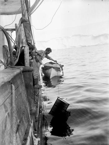 Frank Hurley leaning over the side of a ship washing film in a crate in the water