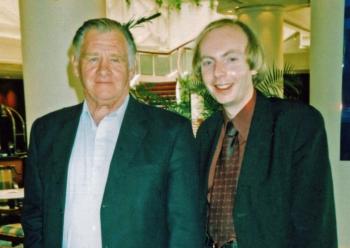 Two men dressed in shirts and suit jackets pictured from the waist up, smiling at camera.