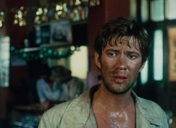 A young man wet with sweat and wearing a grubby suit jacket in a pub