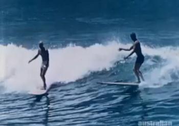 Still frame of two surfers riding a wave.