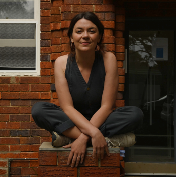 Digital artist and poet Jazz Money sitting cross-legged on a brick wall