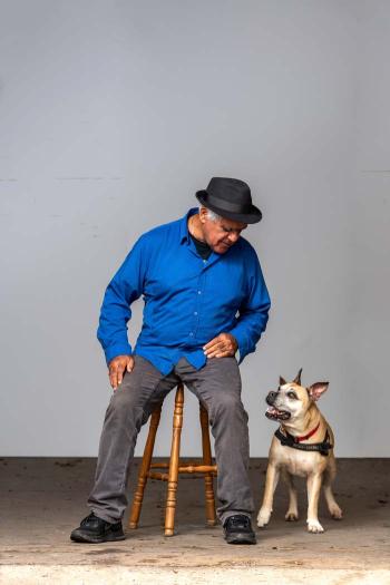 Richard Bell seated on a stool looking down at his dog Tilly, a Staffordshire cross.