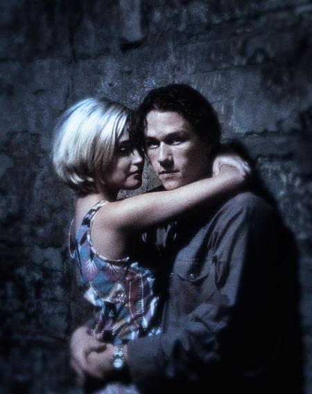 Heath Ledger as Jimmy and Rose Byrne as Alex in a still from Two Hands. The shot is grainy and plays with focus. They are in an embrace while they lean on a wall. Ledger looks at the camera.