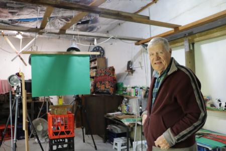 And older man in a studio surrounded by various filmmaking artefacts.
