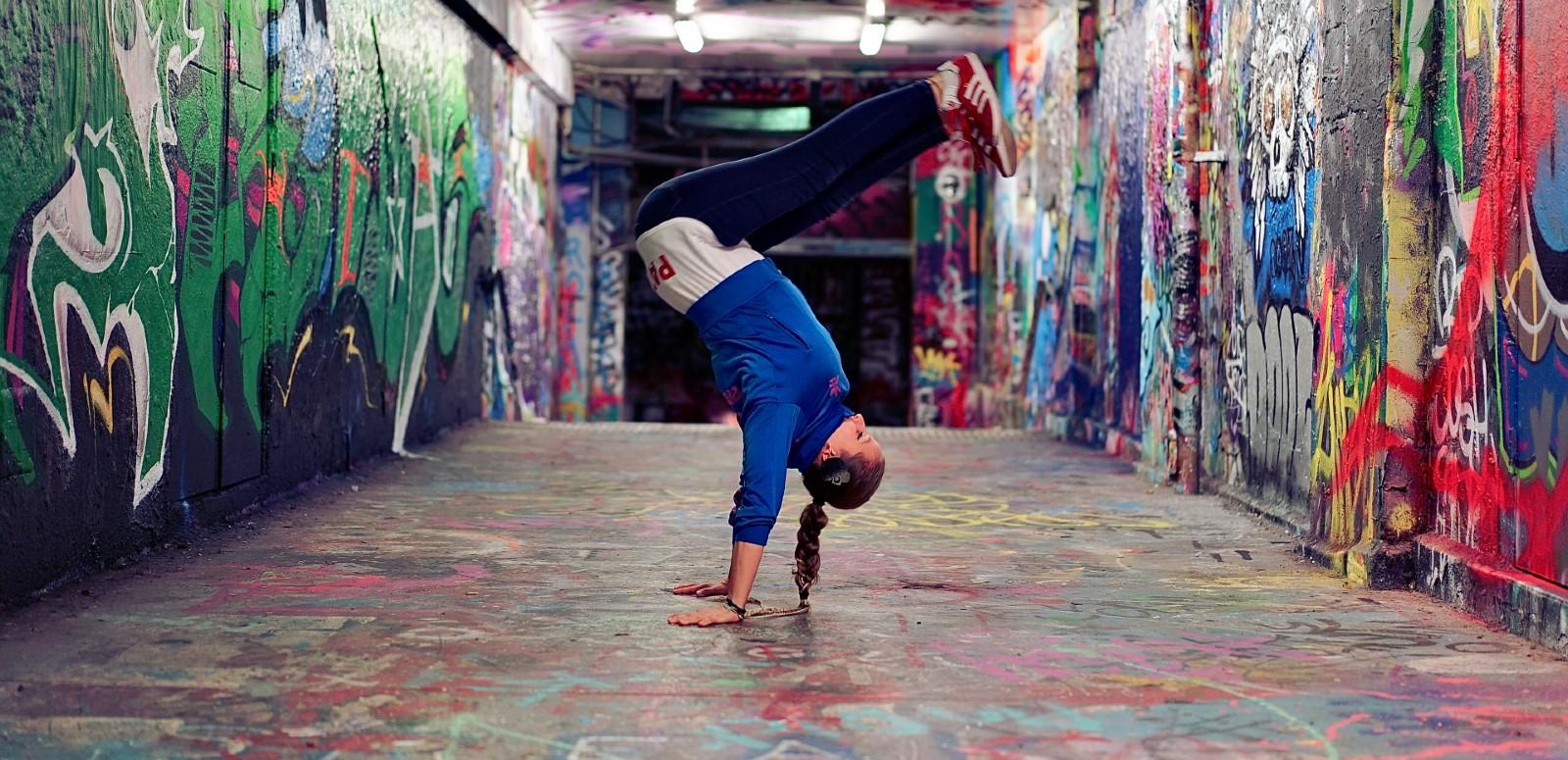 A woman standing on her hands, hip-hop dancing, in a graffitied tunnel
