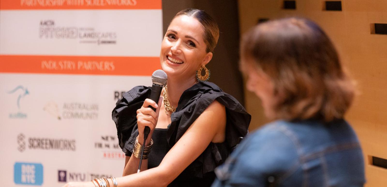 Rose Byrne holds a microphone at an onstage Q&A