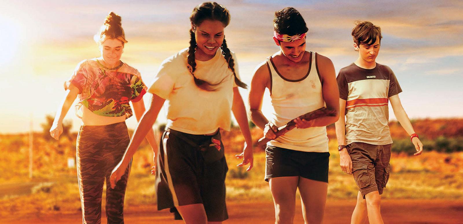 Four teenagers walking along a road in the outback.