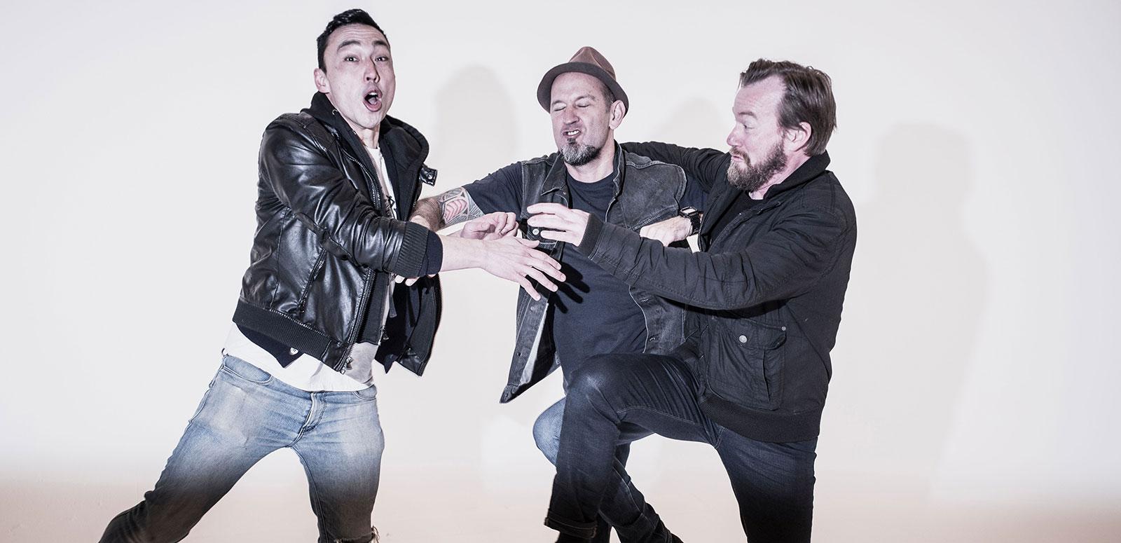Three band members from Regurgitator comically pushing and shoving each other. 