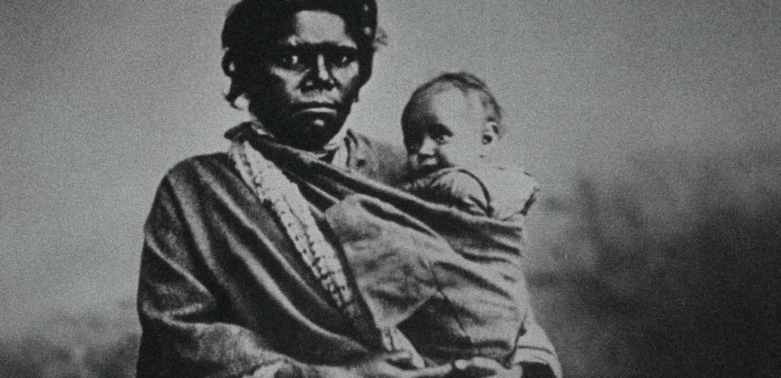 A black-and-white photo dating from the early 20th century of an Indigenous woman holding a baby.