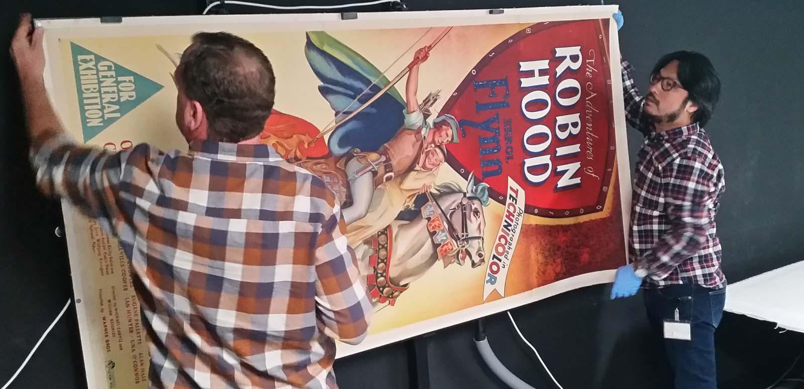 Two NFSA staff members carrying a poster for the film The Adventures of Robin Hood, starring Errol Flynn