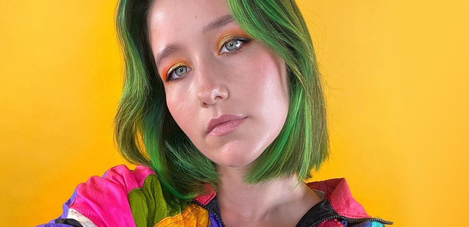 Woman with green hair looking at camera, against a yellow background