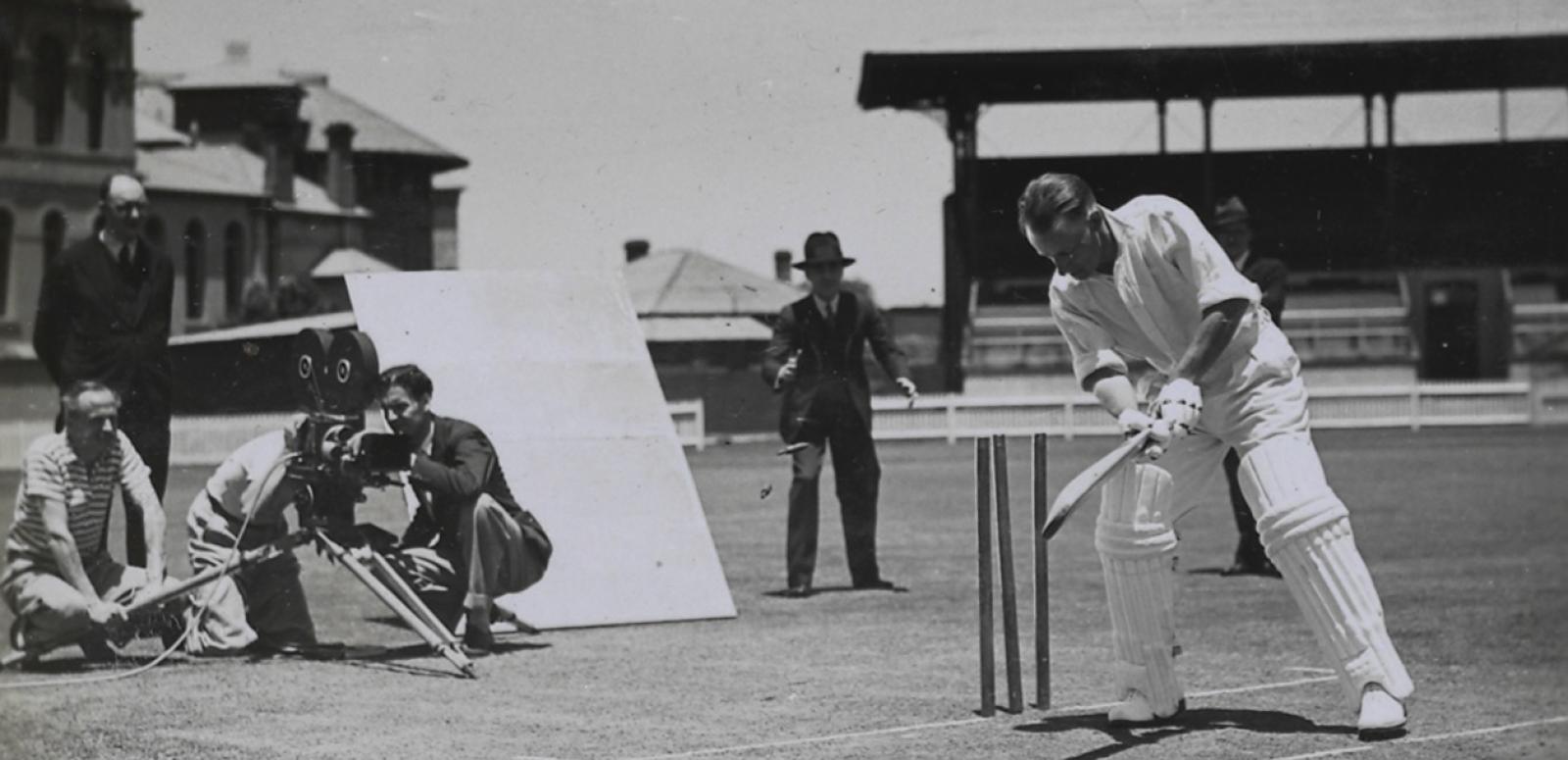 Donald Bradman batting in front of wickets while a film crew films him from behind
