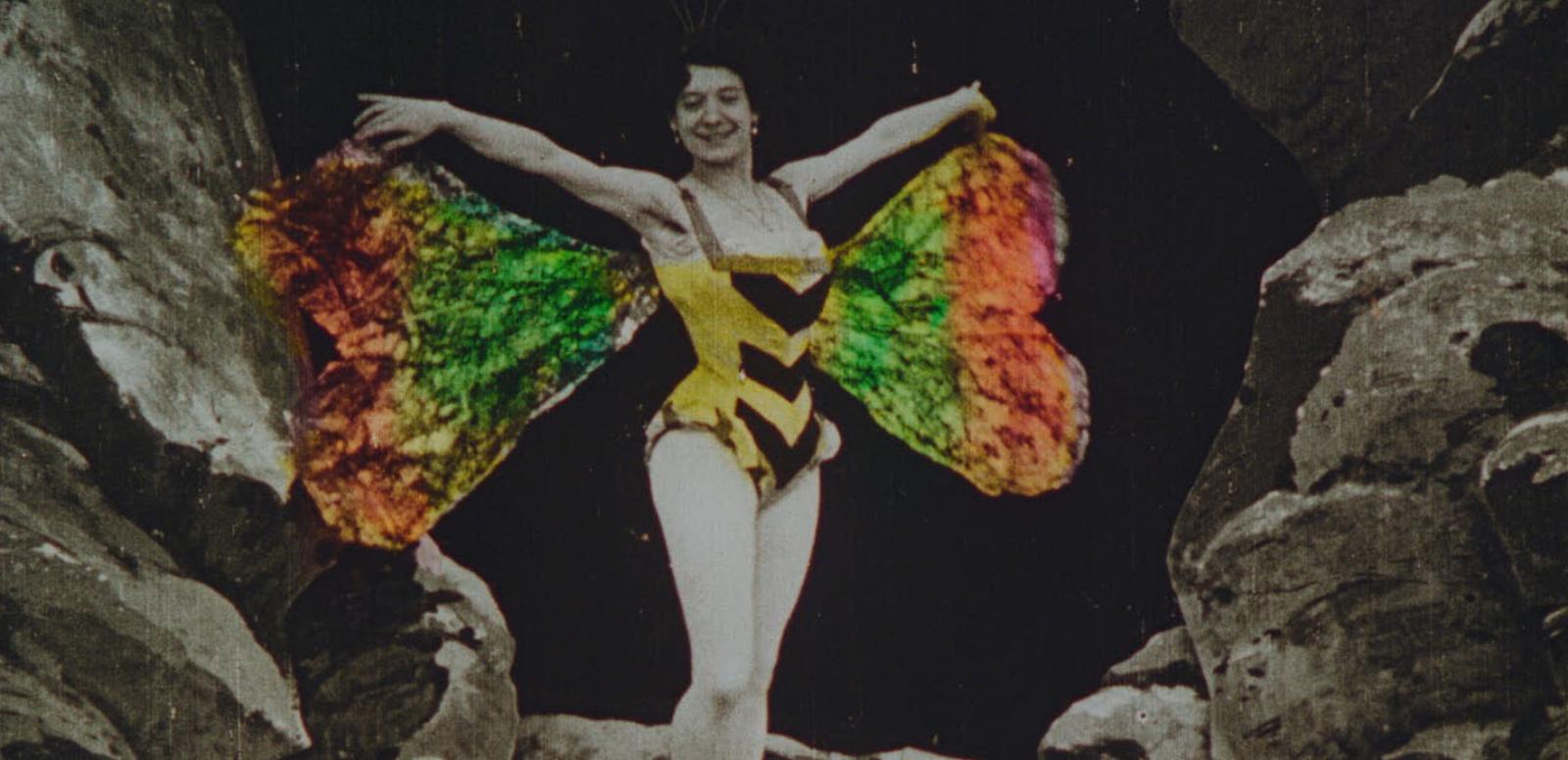 Handcoloured image of  woman wearing a yellow dancer's costume and colourful butterfly wings