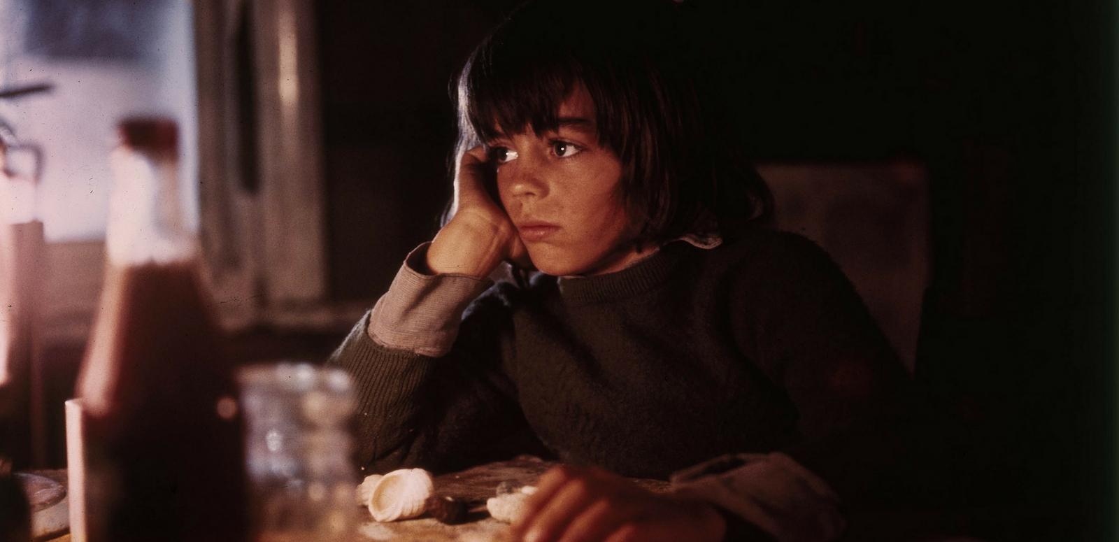 Production still of young Greg Rowe as Storm Boy sitting in his darkened humpy. His face is lit by a lamp.  
