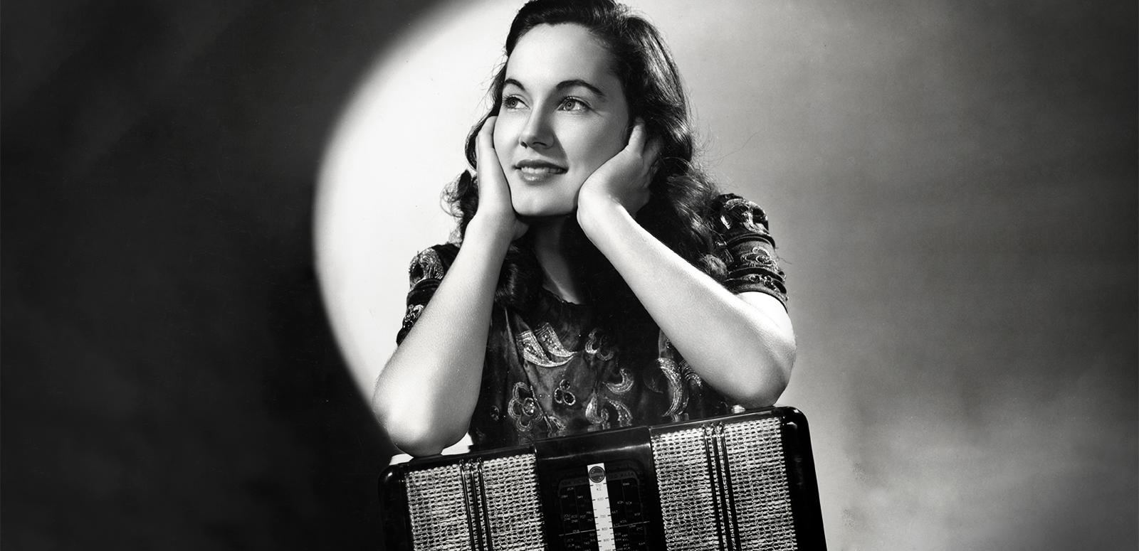 Black and white portrait of actress Betty Bryant wit her elbows resting on a piano accordian and her face in her hands.