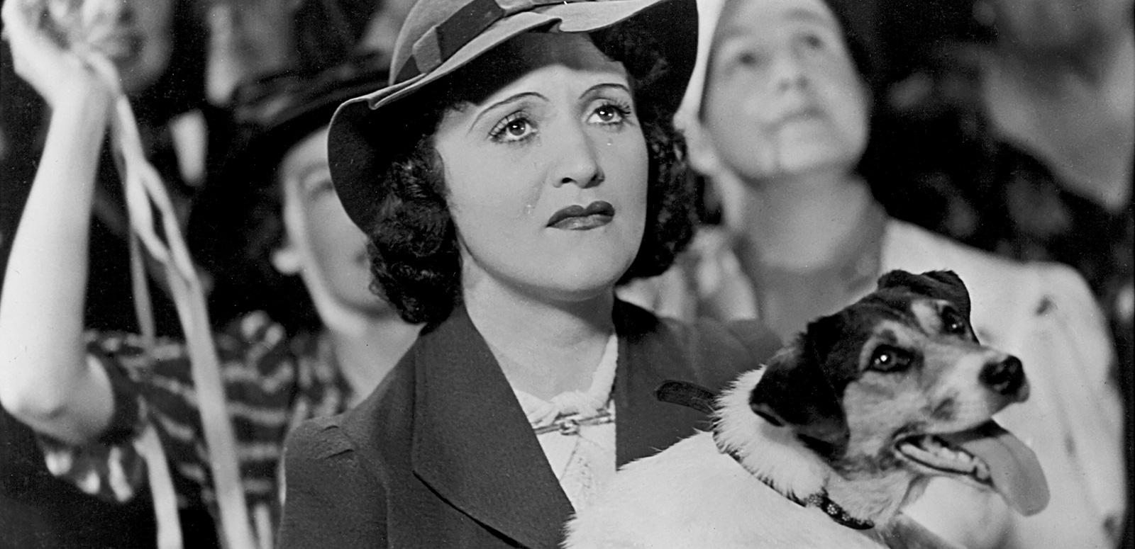 A crying Diana Du Cane holds a dog in her arms and looks upwards at a departing ship in a scene from The Broken Melody