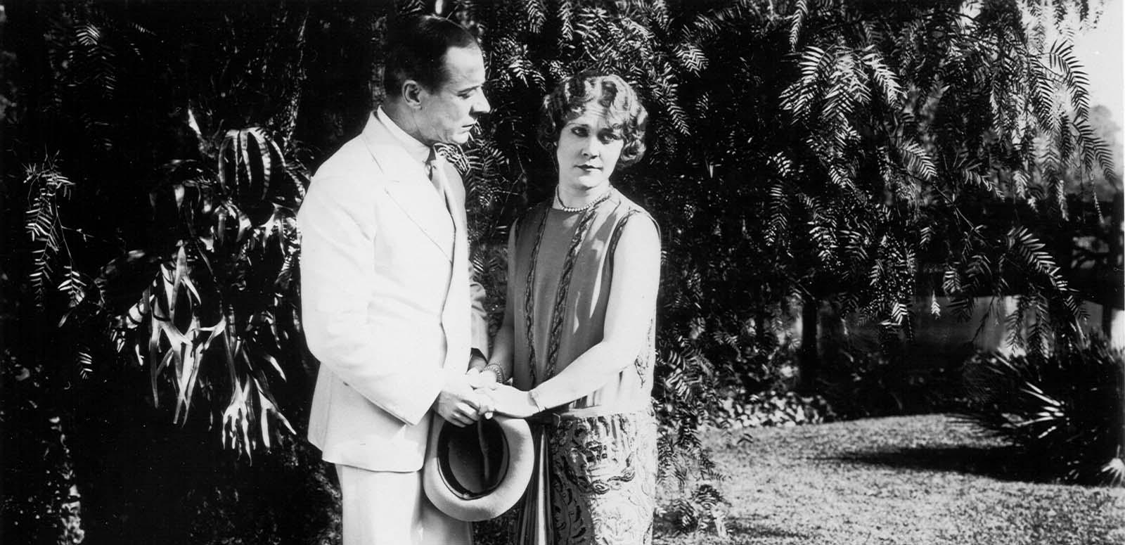 A man holds hands with Louise Lovely in a garden in a scene from the silent film Jewelled Nights.