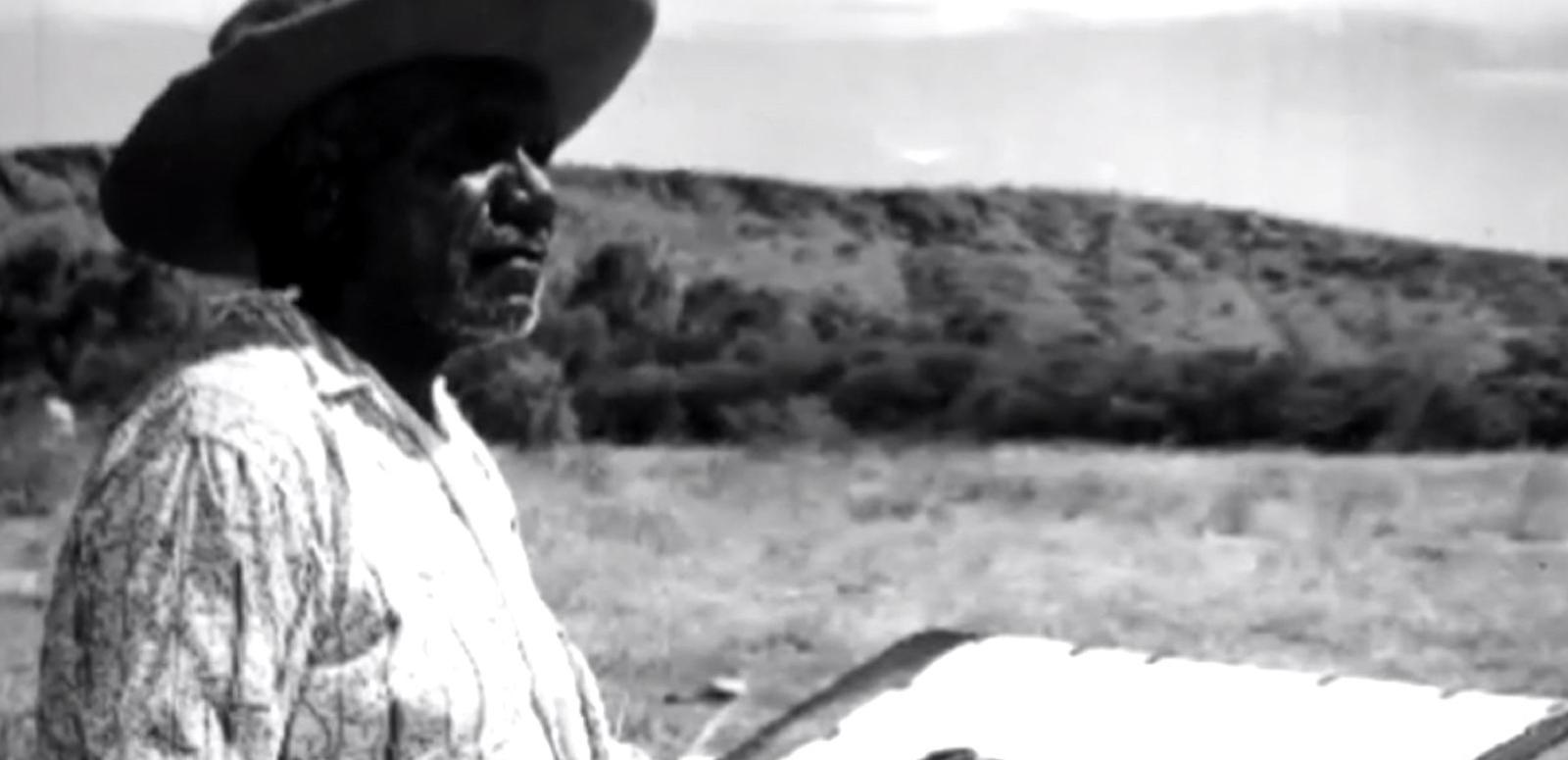 Indigenous artist Albert Namatjira standing in the outback, pictured in profile and looking out at the landscape