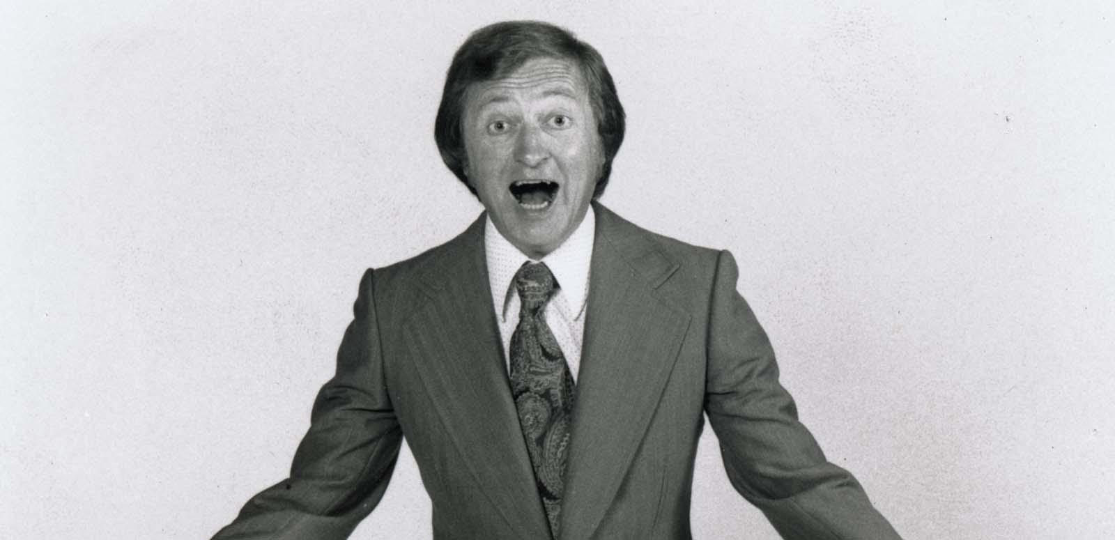 A 1970s publicity shot of Graham Kennedy wearing a suit and exclaiming at the camera.