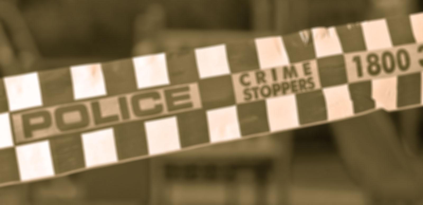 A sepia-toned shot of some checkered police tape with the words Police and Crime Stoppers written on it.