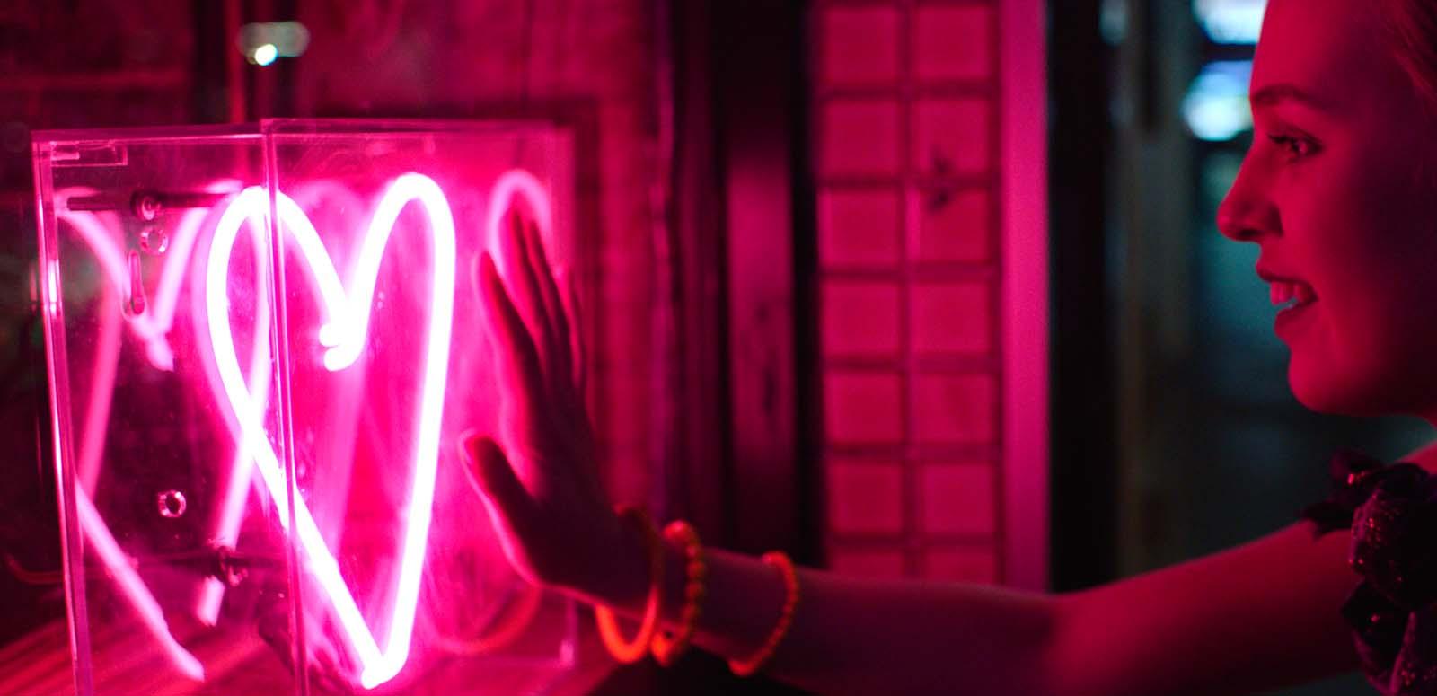 A woman holds out her hand to a neon-lit heart symbol