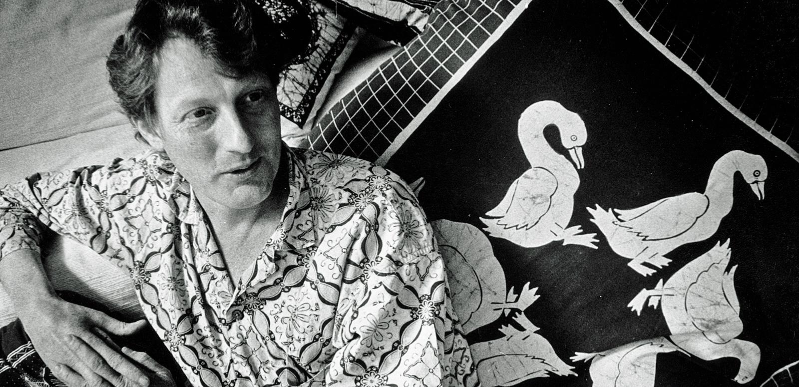 Australian documentary filmmaker, John Darling, pictured from waist up, wearing a Balinese shirt and leading against a cushion with images of birds on it.