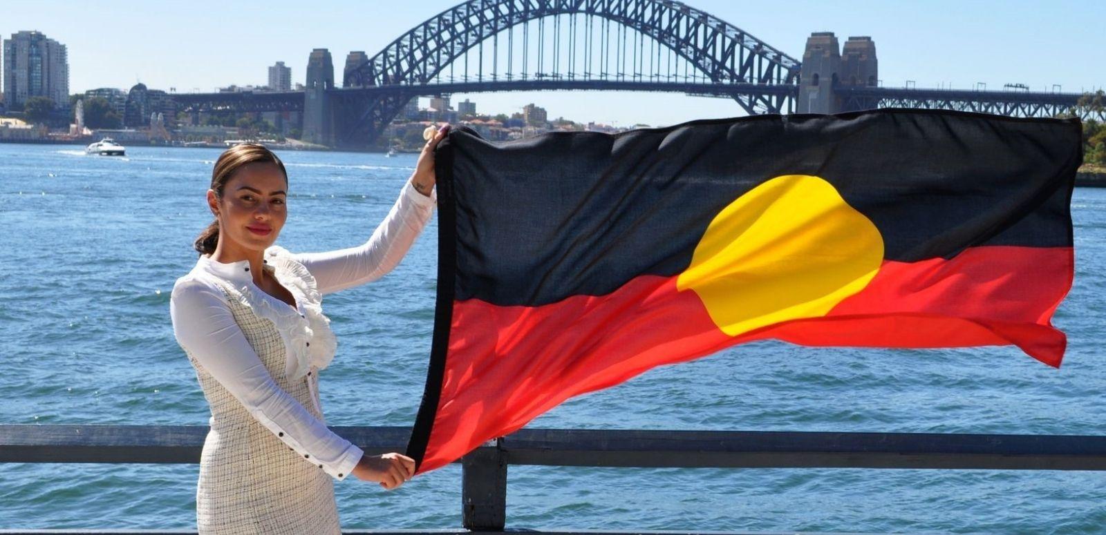 Cheree Toka holding an Australian Aboriginal flag. The Sydney Harbour Bridge is in the background.
