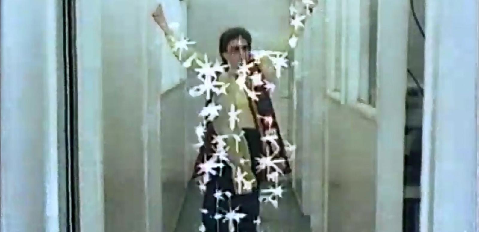 Frame capture of a woman in a hallway with superimposed starbursts across her body