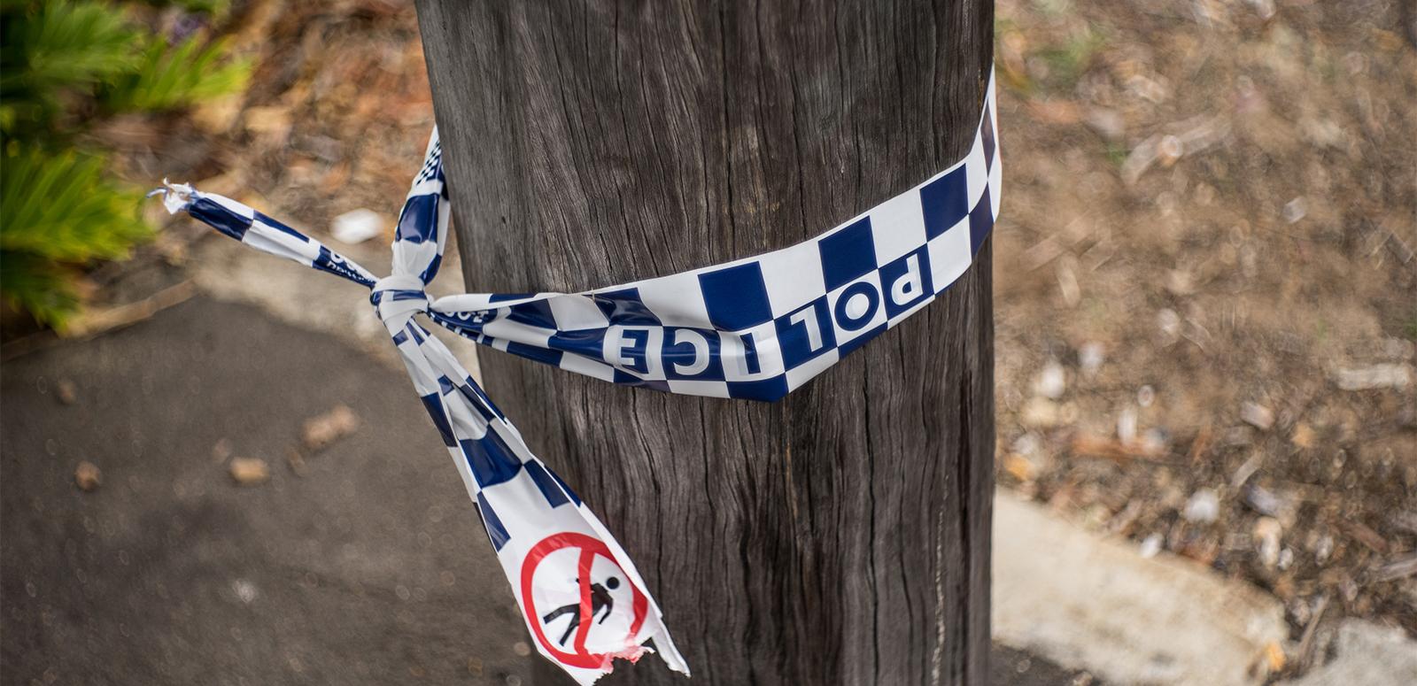A section of a telegraph pole on a sidewalk with some blue and white chequered police tape tied around it.
