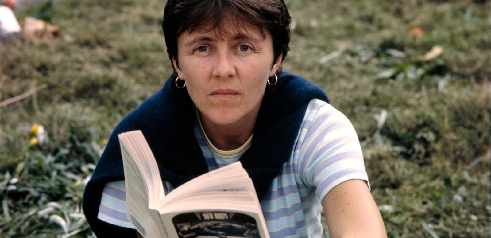 Helen Garner sitting in the ground, look at the camera and holding an open book