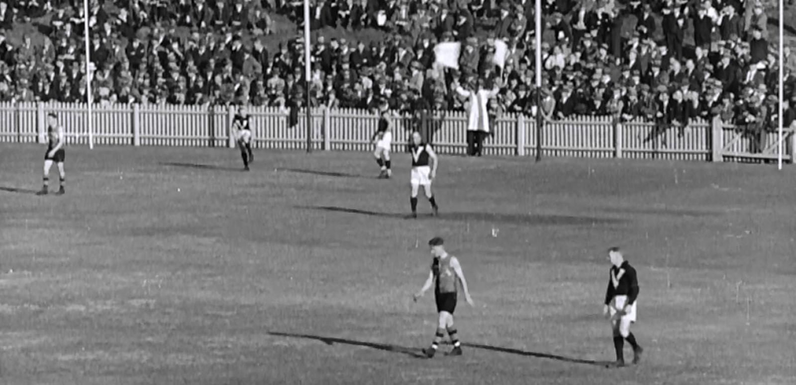 Black and white frame capture of the AFL goal umpire waving two flags signalling a six point score.