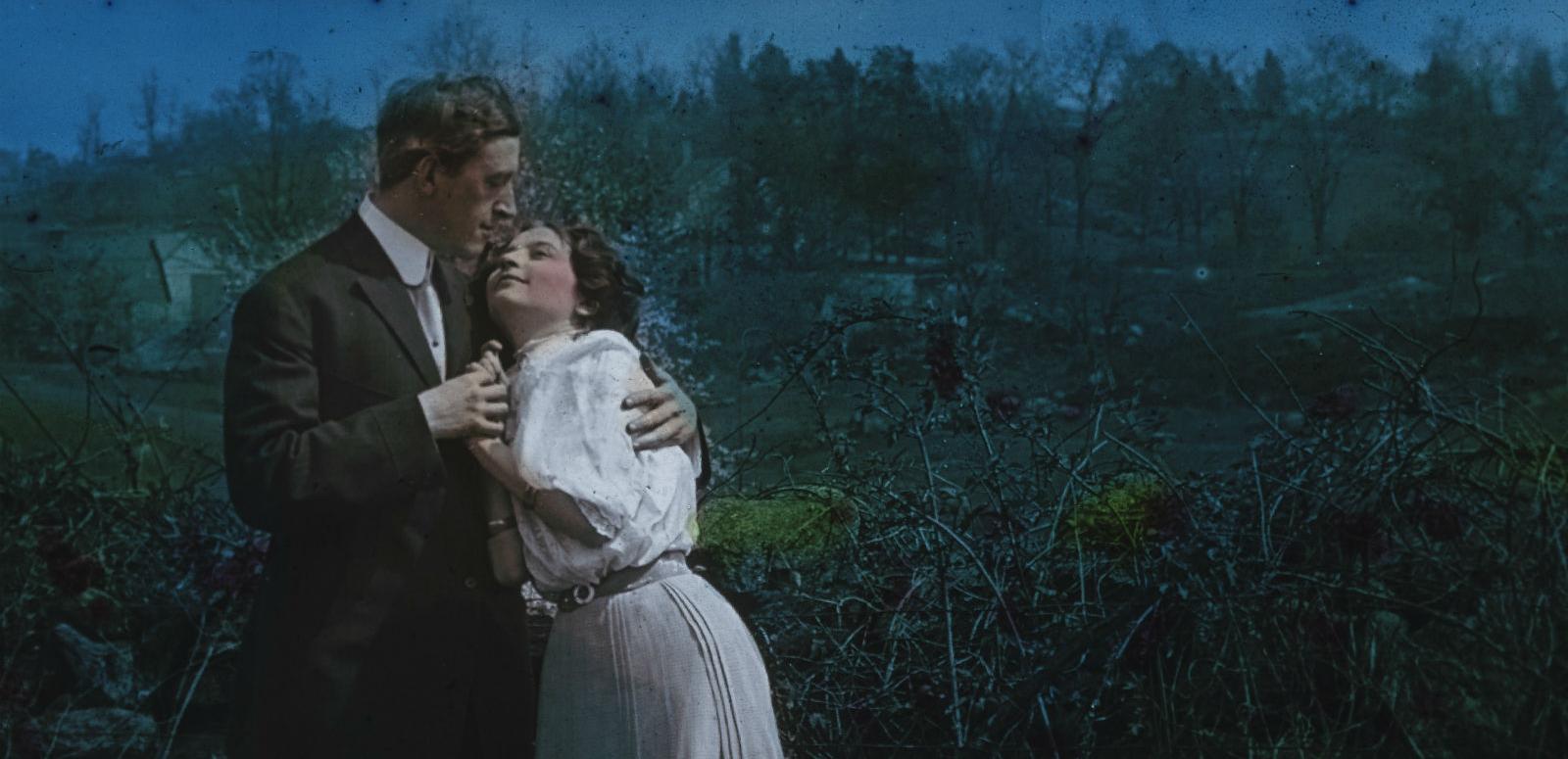 Glass slide image of a man and woman in an embrace standing in the moonlight, circa 1906.
